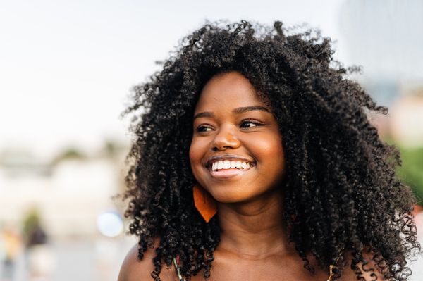 Mulher jove sorridente, de cabelos cacheados longos