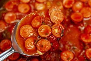 Colher de sopa cheia de salsicha picada com molho vermelho, cebola picada e temperos