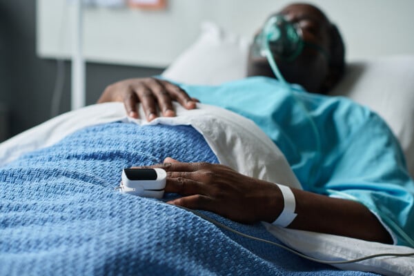 homem deitado em maca de hospital usando máscara de oxigênio com um oxímetro no dedo