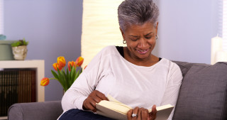 Mulher idosa lendo livro no sofá