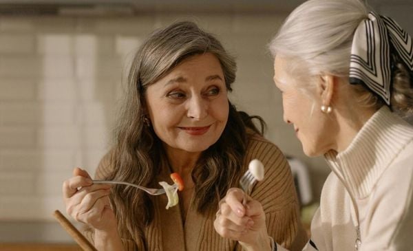 Duas mulheres idosas se olhando enquanto comem frutas com garfo