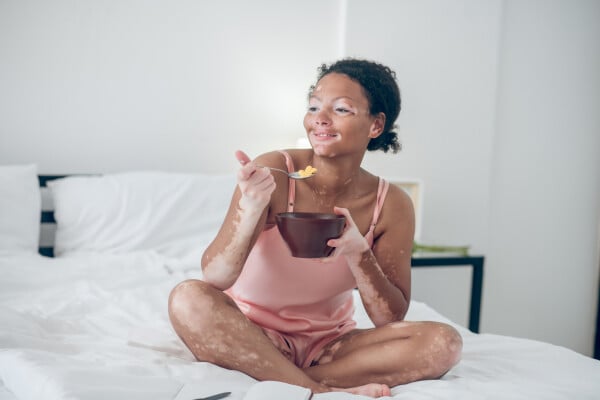 mulher sentada na cama enquanto toma café da manhã