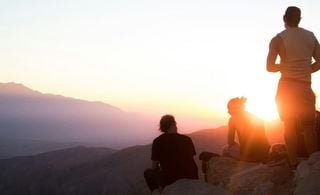 Três pessoas observando o por do sol em uma montanha