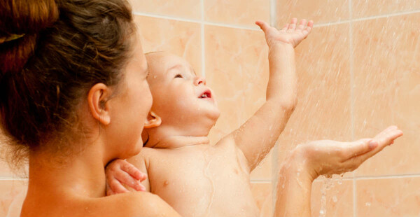 Mãe segurando filho no colo embaixo do chuveiro