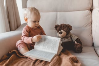 Foto de bebê segurando um livro ao lado de um urso de pelúcia