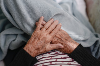 Mãos de mulher idosa em cima de cobertor uma em cima da outra