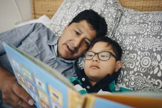 pai e filho lendo livro deitados na cama