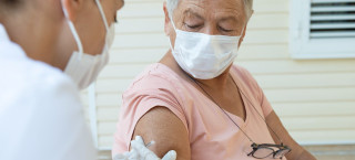 Enfermeira aplicando vacina em mulher idosa