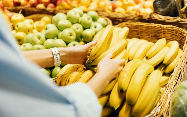 mulher no mercado escolhendo banana e maçã