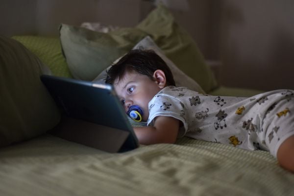 Garotinho deitado em uma cama enquanto assiste algo em um tablet