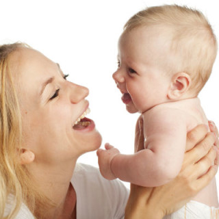 Bebê olhando nos olhos e rindo com a mãe - Foto: Getty Images