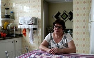 mulher idosa sozinha sentada com os braços sob uma mesa na cozinha