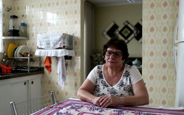 mulher idosa sozinha sentada com os braços sob uma mesa na cozinha