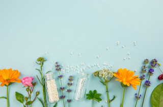 Flores e plantas junto com frascos de comprimidos homeopáticos e comprimidos homeopáticos espalhados
