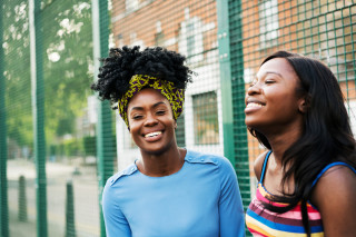 Duas mulheres negras, sentadas uma ao lado da outra, sorrindo