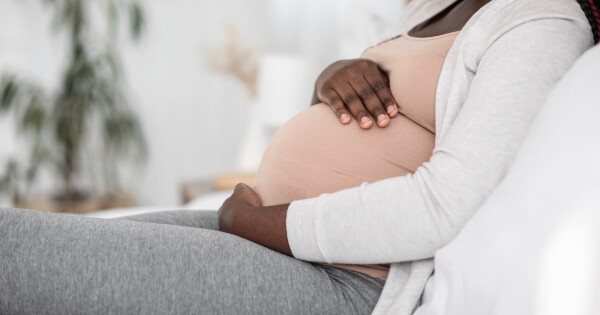 Mulher grávida sentada no sofá com as mãos na barriga