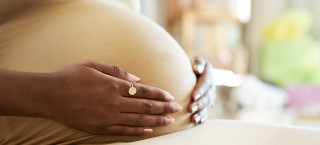 Foto aproximada de mulher negra grávida segurando a barriga