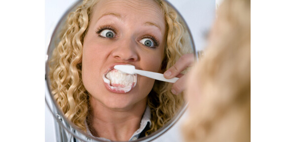 Mulher escovando os dentes em frente ao espelho