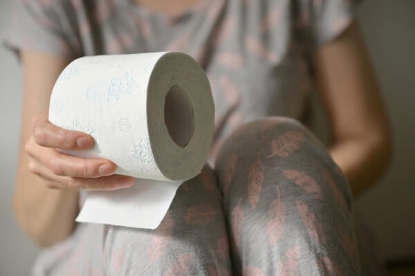 Mulher sentada no vaso sanitário segurando papel higiênico