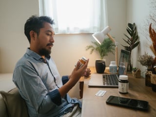 Homem com roupa social sentado na cadeira do escritório e segurando um frasco de medicamento