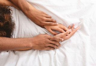 Casal deitado na cama com o homem segurando a mulher pelo braço