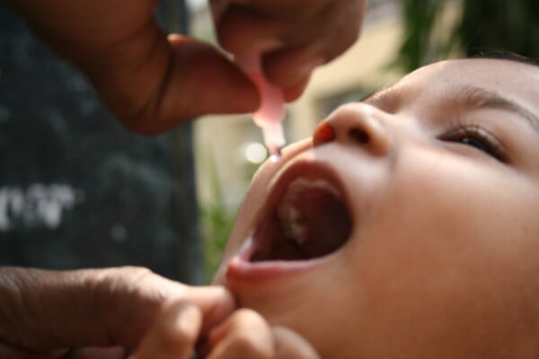 Criança recebendo vacina da poliomielite oral (gotinha) na boca