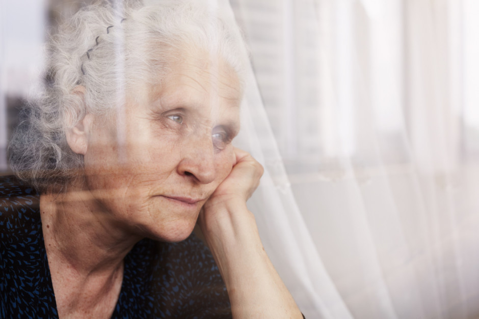 Foto de mulher idosa olhando pensativa pela janela