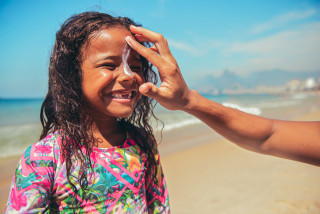 criança na praia aplicando protetor solar facial