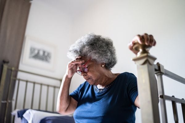 Mulher idosa sentada na cama com a mão na cabeça