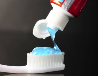 Pasta de dente azul sendo colocada em uma escova branca