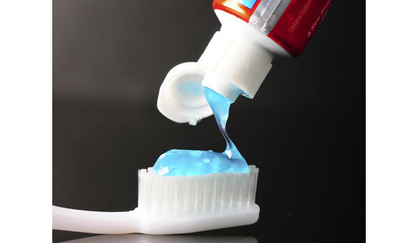 Pasta de dente azul sendo colocada em uma escova branca