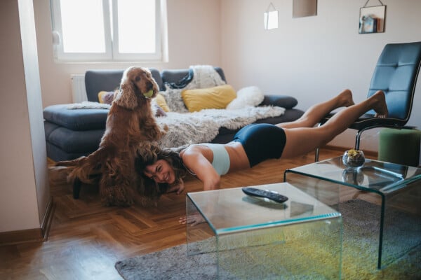 mulher fazendo flexão de braço na sala, com os pés em uma cadeira, com seu cachorro ao lado