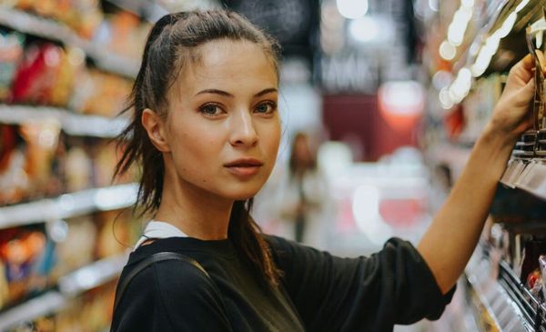 Mulher em um supermercado escolhendo coisas em uma prateleira e olhando para a câmera