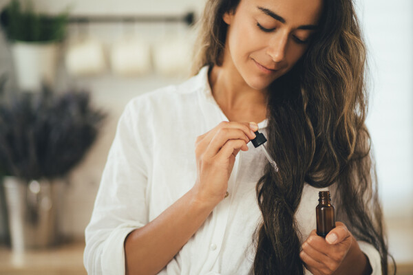 Mulher passando óleo essencial no comprimento do cabelo