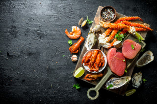 Vista de cima de uma tábua de madeira repleta de frutos do mar, como camarões, lagostas e ostras, além de duas postas de atum; todos eles são alimentos ricos em zinco