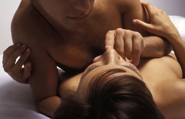 casal abraçado na cama com o homem em cima da mulher tocando a boca dela