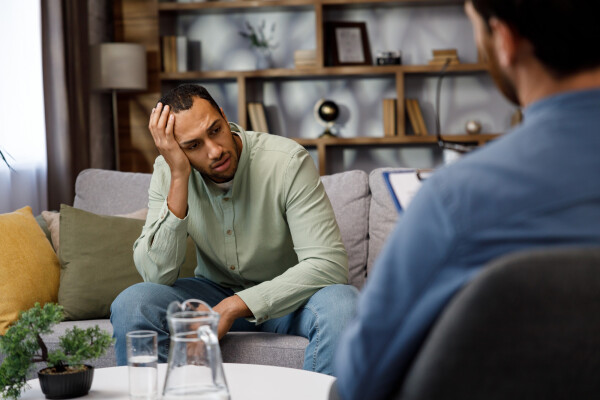 Homem com expressão de preocupação, sentado em um sofá em um consultório durante uma sessão com um psicólogo