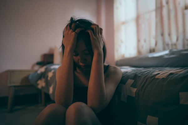 Uma mulher deprimida segurando a testa em um quarto mal iluminado.
