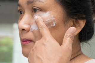 mulher asiática passando creme no rosto