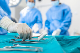 Mão de enfermeira pegando instrumento cirúrgico para grupo de cirurgiões no paciente operacional de fundo no teatro cirúrgico. Instrumentos médicos de aço prontos para serem usados.