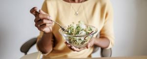 Mulher desfocada segurando uma tigela de salada que está em primeiro plano