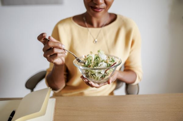 Mulher desfocada segurando uma tigela de salada que está em primeiro plano