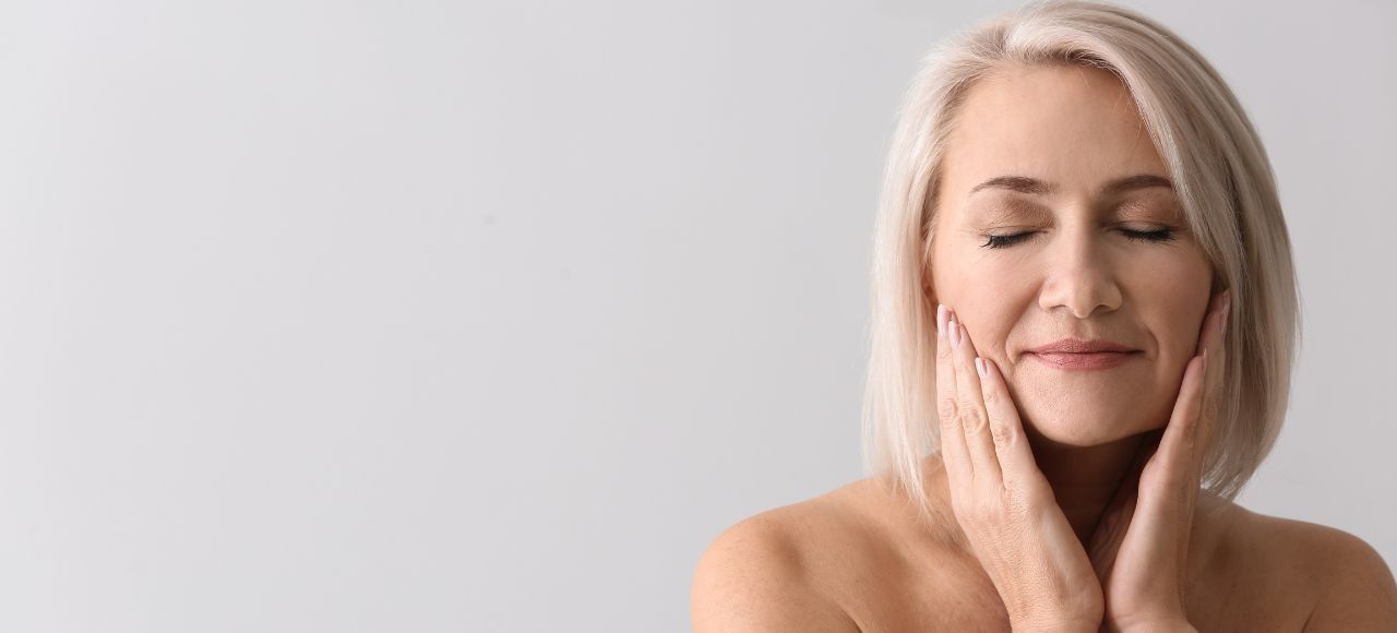 Mulher mais velha fazendo uma massagem facial em si mesma em um fundo iluminado