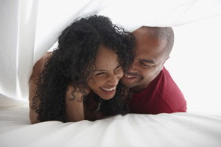 Casal sorrindo se abraçando embaixo dos lençóis