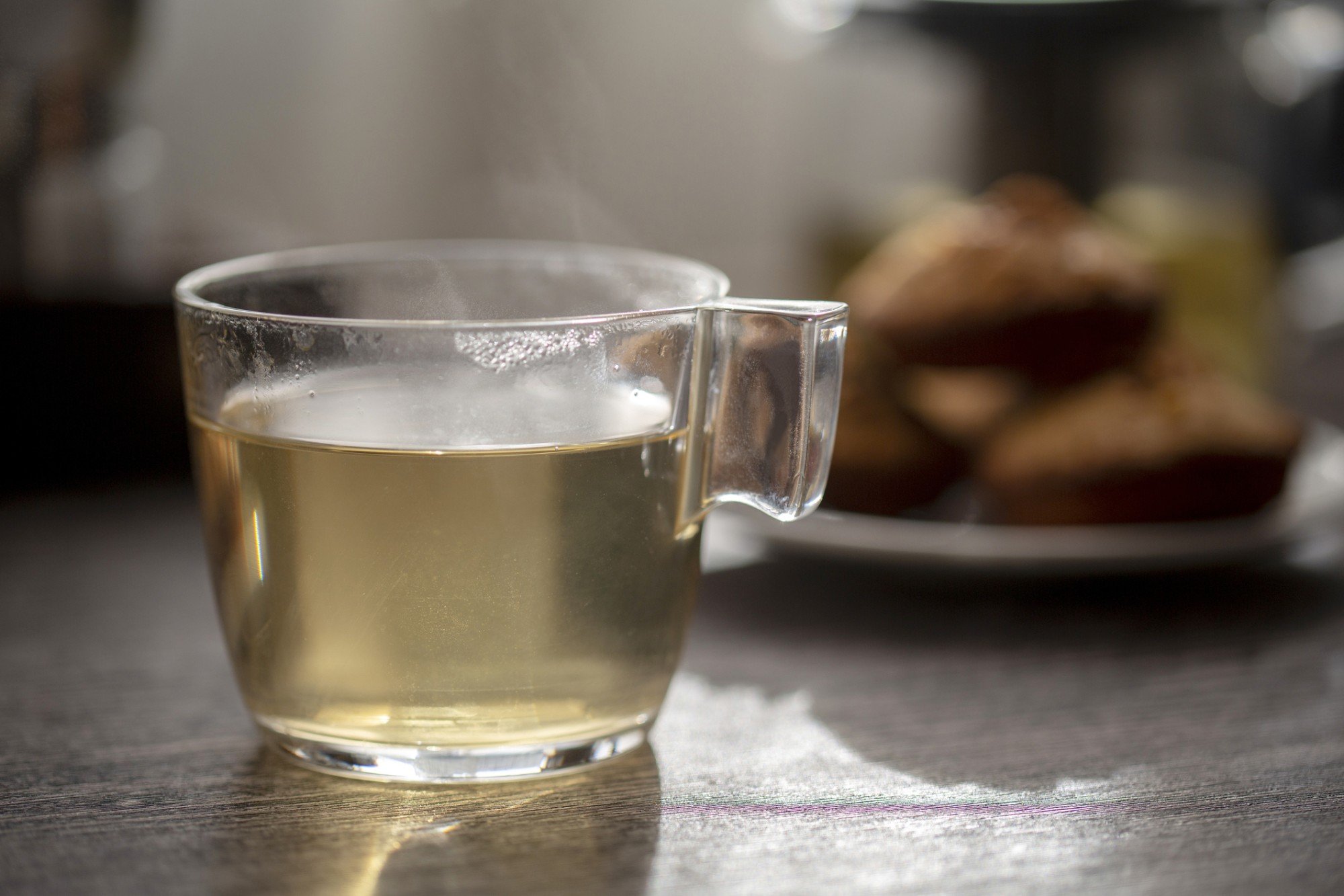 xícara de chá de baleeira em cima de mesa de madeira, com bolinhos de noz caseiro desfocados no fundo da imagem