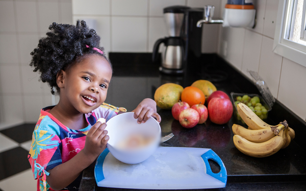 Menina na cozinha comendo frutas em uma tigela