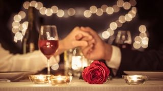 Casal dando as mãos em jantar especial à mesa com taça de vinho e rosa
