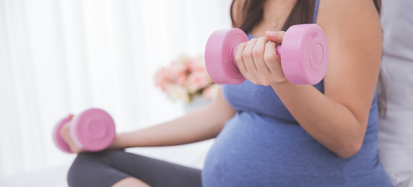 Mulher grávida segura dois halteres nas mãos, praticando musculação