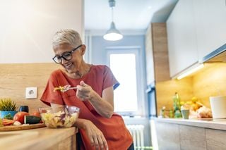 Mulher madura comendo em uma cozinha