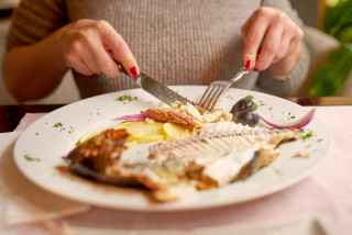 Mulher sentada na mesa comendo peixe no prato